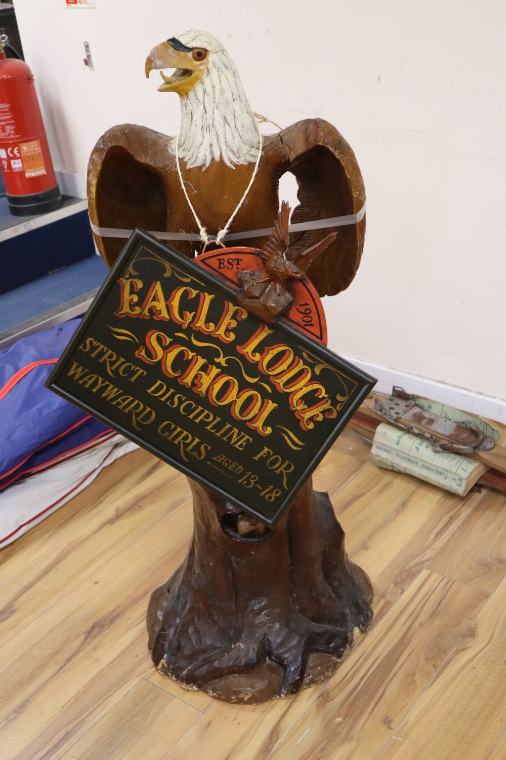A carved and painted wood model of a Bald Eagle perched on a tree stump and a carved and painted wood hanging sign